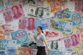 FILE - In this Aug. 6, 2019, file photo, a woman walks by a money exchange shop decorated with different countries currency banknotes at Central, a business district in Hong Kong. China's trade with the United States fell sharply in August as a tariff war that threatens global economic growth worsened. (AP Photo/Kin Cheung, File)
