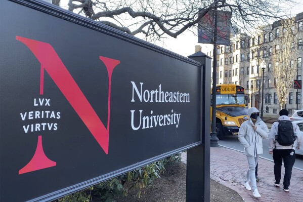 FILE - In this Jan. 31, 2019 file photo, pedestrians walk near a Northeastern University sign on the school's campus in Boston. Steve Waithe, of Chicago, a former track and field coach at Northeastern University accused of setting up sham social media and email accounts in an attempt to trick women into sending him nude or semi-nude photos of themselves pleaded guilty in federal court in Boston, prosecutors said Tuesday, Nov 21, 2023. (AP Photo/Rodrique Ngowi, File)