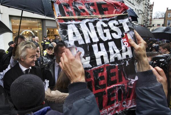FILE - In this March 8, 2017 file photo, a man holds a placard reading "Don't Give Hate And Fear A Vote" as firebrand anti-Islam lawmaker Geert Wilders, left, passes by during a campaign stop in Breda, Netherlands. A Dutch appeals court upheld Friday the conviction of anti-Islam lawmaker Geert Wilders for insulting Moroccans in comments he made at an election night gathering in 2014. He was cleared of incitement to hate and discrimination. (AP Photo/Peter Dejong, File)