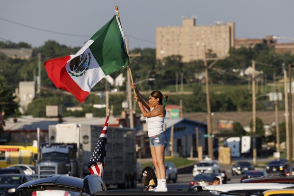 Brila Adauto of Omaha waves a Mexican flag as hundreds gather in after U.S. Immigration and Customs Enforcement conducted a raid earlier in the day in Omaha, Neb. on Tuesday, June 10, 2025. (Nikos Frazier/Omaha World-Herald via AP)