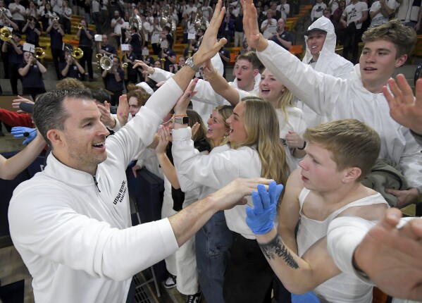 El entrenador en jefe de Utah State, Danny Sprinkle, izquierda, celebra con los estudiantes después de derrotar a San Jose State en un partido de baloncesto universitario de la NCAA el martes 30 de enero de 2024 en Logan, Utah.  (Eli Lucero/The Herald Journal vía AP)
