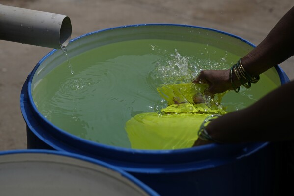A resident of Ambedkar Nagar, a low-income settlement in the shadows of global software companies in Whitefield neighborhood, collects potable water from a private tanker in Bengaluru, India, Monday, March 11, 2024. Bengaluru is witnessing an unusually hot February and March, and in the last few years, it’s received little rainfall in part due to human-caused climate change. (AP Photo/Aijaz Rahi)