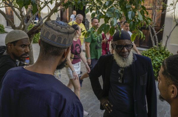 Muslims speak in front of their mosque as tourists, wearing Ernesto "Che" Guevara T-shirts, walk past in Havana, Cuba, Friday, Feb. 16, 2024. The only mosque in Havana opened in 2015 and the Muslim community has grown to about 2,500 people nationwide. (AP Photo/Ramon Espinosa)