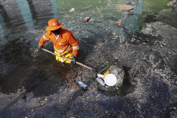 A city worker picks trash from a street flooded by the waters of the Negro River in downtown Manaus, Brazil, May 20, 2021. (AP Photo/Edmar Barros)