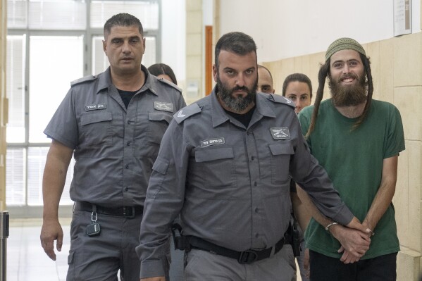 Elisha Yered, 22, right, is led handcuffed by officers during an appearance at the Jerusalem District Court on Tuesday, Aug. 8, 2023. Yered is one of two Israeli settlers arrested on suspicion of involvement in the killing of a Palestinian man in the West Bank on Friday. (AP Photo/Ohad Zwigenberg)