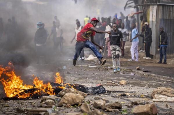 A protester jumps in the air as he throws a rock towards police next to a burning barricade in the Kibera slum of Nairobi, Kenya, Monday, March 20, 2023. Hundreds of opposition supporters have taken to the streets of the Kenyan capital over the result of the last election and the rising cost of living, in protests organized by the opposition demanding that the president resigns from office. (AP Photo/Ben Curtis)