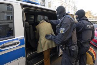 FILE - Masked police officers lead an arrested suspect, left, to a police vehicle during a raid against so-called 'Reich citizens' in Frankfurt, Germany, Wednesday, Dec. 7, 2022. The number of politically motivated crimes reported in Germany rose by 7% last year, Germany’s top security official said Tuesday, May 9, 2023. (Boris Roessler/dpa via AP, File)
