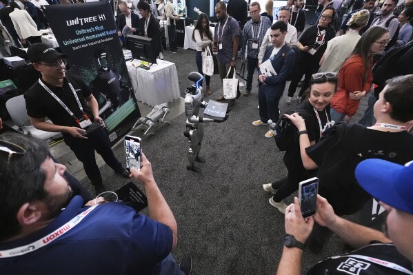 A human-like Unitree robot is surrounded by convention guests while passing out company brochures at the Robotics Summit & Expo, Wednesday, April 30, 2025, in Boston. (AP Photo/Charles Krupa)