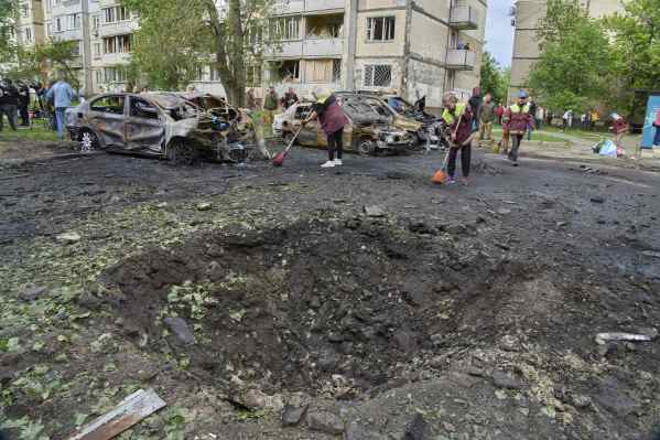 Municipal workers clean up near burnt cars and a crater made by a drone in the residential area following Russia's air raid in Kyiv, Ukraine, Sunday, May 4, 2025. (AP Photo/Efrem Lukatsky)