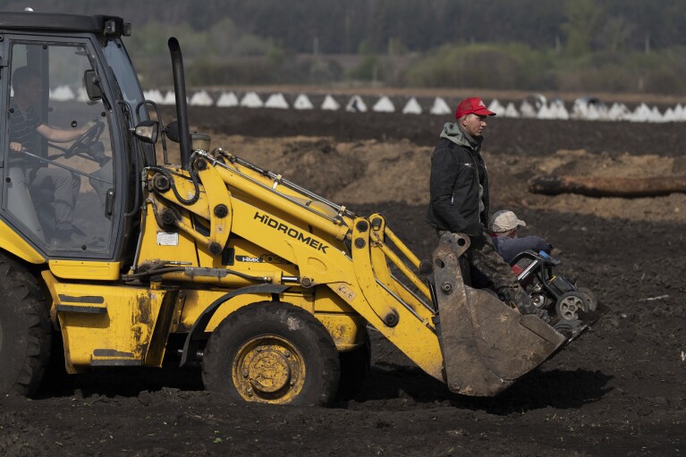 Workers ride by an excavator to construct new defensive positions close to the Russian border in the Kharkiv region, Ukraine, on Wednesday, April 17, 2024. (AP Photo/Evgeniy Maloletka)