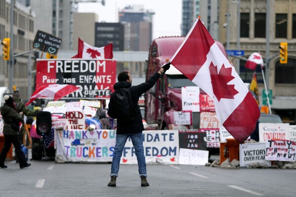 FILE - A protester waves a Canadian flag in front of parked vehicles at a protest against COVID-19 measures that has grown into a broader anti-government protest, in Ottawa, Ontario, Feb. 11, 2022. In a decision released Tuesday, Jan. 23, 2024, a Canadian judge ruled that the government’s use of the Emergencies Act to quell weeks of protests by truckers and others angry over COVID-19 restrictions in 2022 was unreasonable and unconstitutional. (Justin Tang/The Canadian Press via AP, File)