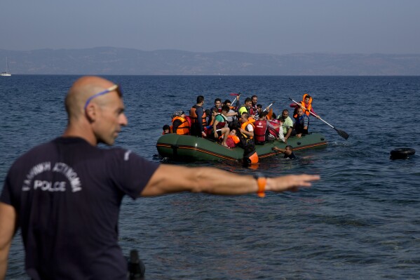 A Greek policeman gives instructions as migrants whose boat stalled at sea while crossing from Turkey to Greece approach the shore of the island of Lesbos, Greece, on Sunday, Sept. 20, 2015. (AP Photo/Petros Giannakouris, File)