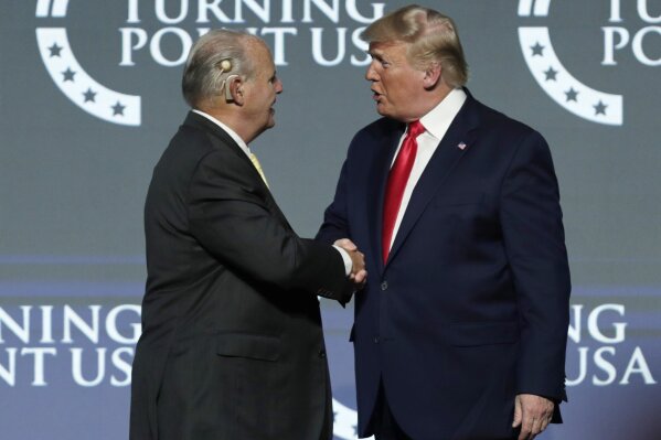 FILE - Rush Limbaugh, left, shakes hands with President Donald Trump as he introduces Trump at the Turning Point USA Student Action Summit at on Dec. 21, 2019, in West Palm Beach, Fla. Limbaugh died of lung cancer on Wednesday, Feb. 17, 2021, four weeks after Trump left office. He was memorialized as the "greatest of all time" on Fox's website, but to critics who saw Limbaugh as a spreader of bigotry, it was good riddance. Limbaugh remained at the top of the heap among radio hosts even until his death. (AP Photo/Luis M. Alvarez, File)
