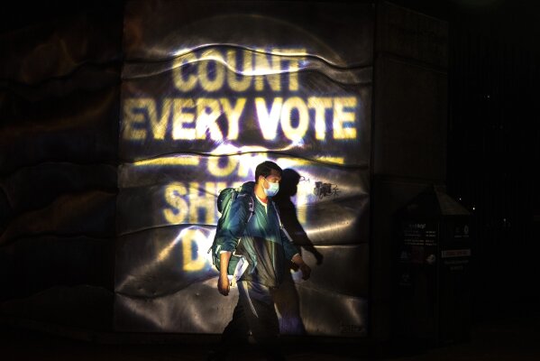 A man walks through a projected election slogan during protests following the Nov. 3 presidential election in Portland, Or. Wednesday, Nov. 4, 2020. (AP Photo/Paula Bronstein)
