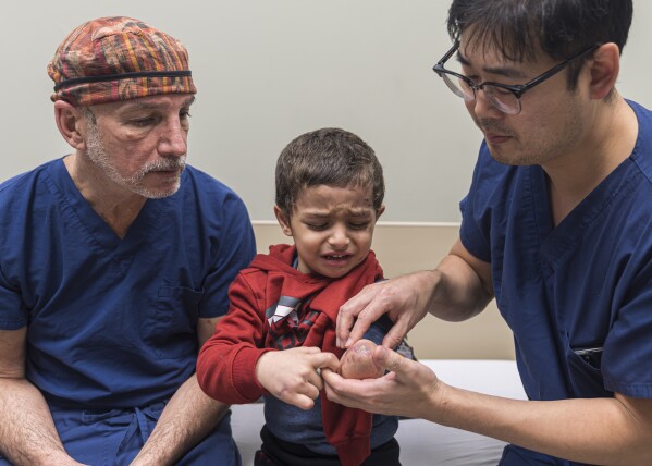Plastic surgeon Dr. Eugene Park and orthopedic surgeon Dr. Scott Kozin examine the arm of 4-year-old Omar Abu Kuwaik at Shriners Children's Hospital on Wednesday, Feb. 28, 2024, in Philadelphia. (AP Photo/Peter K. Afriyie)