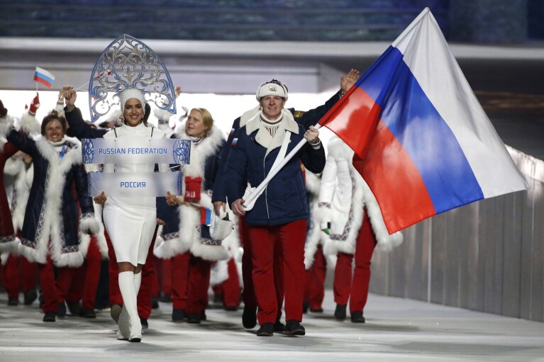 FILE - Bobsledder Alexander Zubkov carries the Russian flag next to model Irina Shayk holding the country’s identification sign at the opening ceremony of the 2014 Winter Olympics in Sochi, Russia, on Feb. 7, 2014. The Sochi Olympics were a pet project of President Vladimir Putin as he sought to project Russia’s global clout, boost its prestige and impress the world. But the Kremlin’s attempt at soft power soon collided with hard realities. (AP Photo/Mark Humphrey, File)
