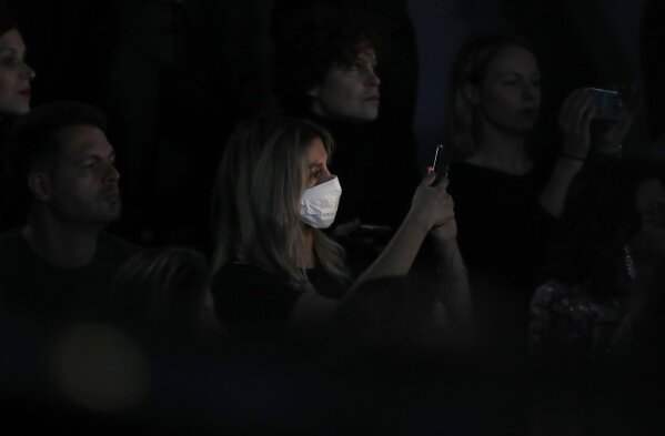 FILE - In this Feb. 23, 2020, file photo, a woman wearing a sanitary mask takes photos during the Dolce & Gabbana women's fall-winter 2020-21 show, in Milan, Italy. Italian Premier Giuseppe Conte's decision to lock down his entire country brought some welcome clarity to life in Italy after weeks of uncertainty about how to behave in a time of coronavirus, according to Associated Press reporter Colleen Barry. (AP Photo/Antonio Calanni, File)