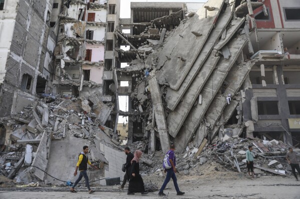 ARCHIVO - Palestinos caminan frente a edificios impactados por ataques israelíes en Ciudad de Gaza, el viernes 24 de noviembre de 2023. (AP Foto/Mohammed Hajjar)