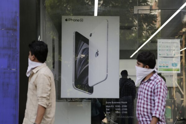 FILE - In this Saturday, Aug. 1, 2020, file photo, people walk past an image of an iPhone displayed at an Apple store in Ahmedabad, India. Apple announced Friday, Sept. 18, that it will launch its first online store in India next week, as it seeks to increase sales in one of the world’s fastest-growing smartphone markets. The company at present uses third-party online and offline retailers to sell its products in the country. (AP Photo/Ajit Solanki, File)