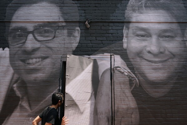 FILE - A woman steps through a door that is covered by a mural depicting American hostages and wrongful detainees who are being held abroad, Wednesday, July 20, 2022, in the Georgetown neighborhood of Washington. At left is Siamak Namazi, who has been in captivity in Iran since 2015. At right is Jose Angel Pereira, who has been imprisoned in Venezuela since 2017. Iran has transferred five Iranian-Americans from prison, identifying three of the prisoners as Siamak Namazi, Emad Shargi, and Morad Tahbaz, to house arrest. The move comes after Tehran has spent months suggesting a prisoner swap with Washington. (AP Photo/Patrick Semansky, File)