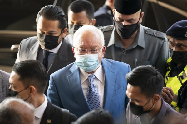 Former Malaysian Prime Minister Najib Razak, center, wearing a face mask arrives at Kuala Lumpur High Court in Kuala Lumpur, Malaysia, Thursday, Feb. 18, 2021. The court Thursday ordered Najib's wife Rosmah Mansor to enter her defense in a corruption trial linked to a 1.25 billion ringgit ($310 million) solar energy project. The ruling was a blow just months after Najib was found guilty in the first of several corruption trials and sentenced to 12 years in jail, pending an appeal. (AP Photo/Vincent Thian)