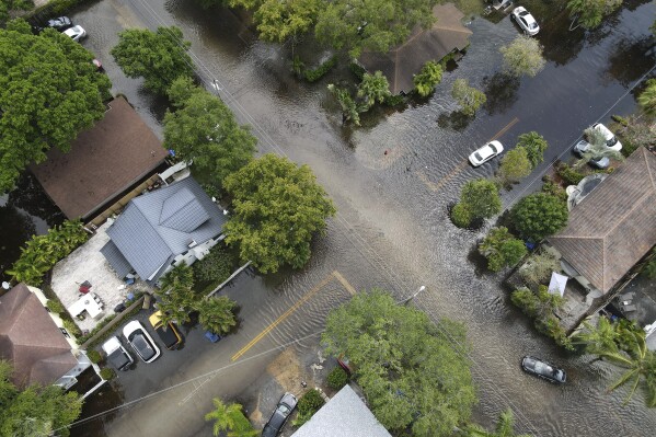 FILE - A pair of waterlogged cars sit abandoned in the road as floodwaters recede in the Sailboat Bend neighborhood of Fort Lauderdale, Fla., April 13, 2023. Flood risk and climate change are pushing millions of people to move from their homes, according to a new study by the risk analysis firm First Street Foundation. (AP Photo/Rebecca Blackwell, File)
