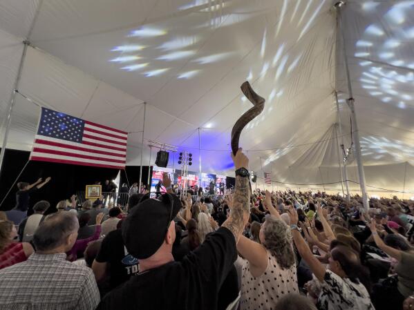 A man holds up a shofar as the audience prays inside a tent during the ReAwaken America Tour at Cornerstone Church in Batavia, N.Y., Friday, Aug. 12, 2022. The instrument, used in some Jewish worship services, has been adopted by the far right, and several people blew the horns to open the conference. (AP Photo/Carolyn Kaster)
