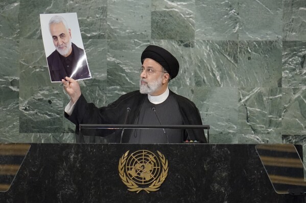 FILE - President of Iran Ebrahim Raisi holds up a photo of slain Iranian Gen. Qassem Soleimani, as he addresses the 77th session of the United Nations General Assembly, Sept. 21, 2022 at U.N. headquarters. Raisi, a hard-line protégé of the country's supreme leader who helped oversee the mass executions of thousands in 1988 and later led the country as it enriched uranium near weapons-grade levels and launched a major drone-and-missile attack on Israel, has died in a helicopter crash according to state media on Monday, May 20, 2024. (AP Photo/Mary Altaffer, File)