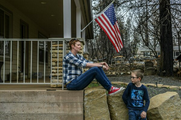 
              In this photo taken March 19, 2019, Dawn Herr and her son Liam, 8, visit their home in Paradise, Calif., that survived the Camp Fire. The Herrs' home, built in 2010, was scorched and had smoke damage inside so the family is living temporarily in nearby Chico. The Herrs credit the home’s survival to strict building codes and to gravel that encircled the building and kept the flames back. (Hector Amezcua/The Sacramento Bee via AP)
            