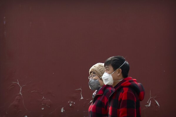 People wearing face masks walk through a public park in Beijing, Friday, Feb. 21, 2020. China reported a further fall in new virus cases to 889 on Friday as health officials expressed optimism over containment of the outbreak that has caused more than 2,200 deaths and is spreading elsewhere. (AP Photo/Mark Schiefelbein)