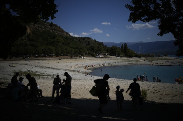 Bathers seek shade on the banks of the receding Sainte-Croix lake, southern France, Tuesday, Aug. 9, 2022. Human-caused climate change is lengthening droughts in southern France, meaning the reservoirs are increasingly drained to lower levels to maintain the power generation and water supply needed for nearby towns and cities. (AP Photo/Daniel Cole)