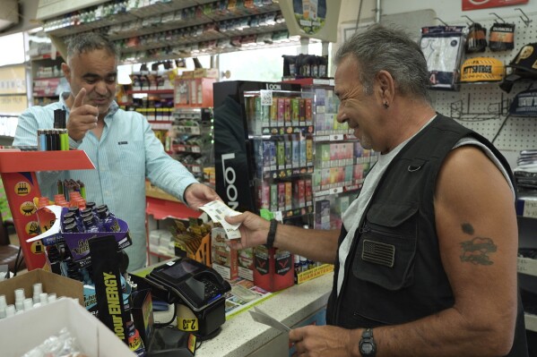 Vinnie Clemente, right, buys Powerball tickets from Elias Harv at a gas station, on Friday, July 14, 2023, in Crystal, Minn. Harv said he’s seen a surge in customers buying lottery tickets as Powerball and Mega Millions jackpots reached $875 million and $560 million respectively. (AP Photo/Mark Vancleave)