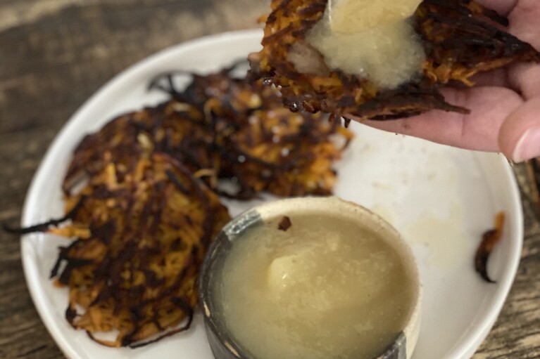 This image provided by Katie Workman shows apple sauce being poured over ginger sweet potato pancakes. (Katie Workman via AP)