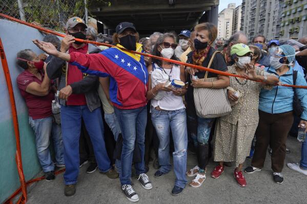 FILE - In this Sept. 16, 2021, file photo, residents stand behind a strip of tape serving as a barrier as they gather outside a vaccination center looking to be inoculated with a second dose of the Sputnik V COVID-19 vaccine, in Caracas, Venezuela. Millions from Latin America to the Middle East are waiting for promised doses of the Russian-made Sputnik V coronavirus vaccine due to manufacturing problems and other issues. (AP Photo/Ariana Cubillos, File)