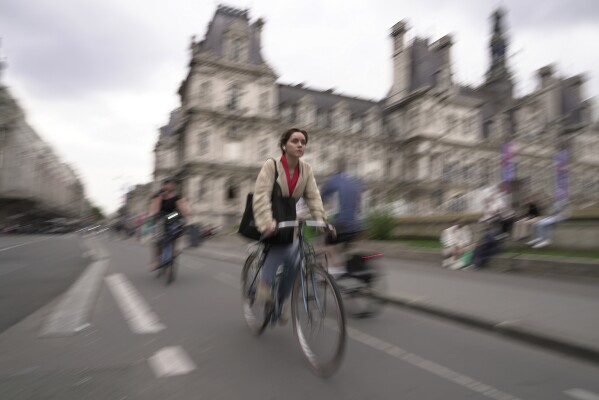 A woman rides past Paris city hall, in Paris, Wednesday, Sept. 13, 2023. (AP Photo/John Leicester)