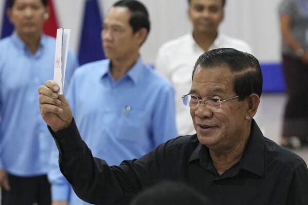 FILE - Cambodian former Prime Minister Hun Sen, foreground, of ruling Cambodian People's Party, shows off a ballot paper before voting for senate election at Takhmau polling station in Kandal province, southeast of Phnom Penh, Cambodia, Sunday, Feb. 25, 2024. The National Election Committee on Monday, Feb. 26, began releasing results by constituency, after earlier announcing that according to a provisional overall count, the Cambodian People’s Party won 55 of the 58 seats that were contested on Sunday. (AP Photo/Heng Sinith, File)