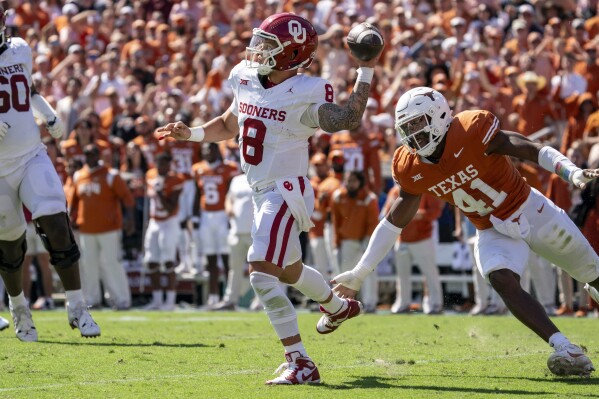 Oklahoma quarterback Dillon Gabriel (8) throws as he escapes from Texas linebacker Jaylan Ford (41) during the first half of an NCAA college football game at the Cotton Bowl, Saturday, Oct. 7, 2023, in Dallas. (AP Photo/Jeffrey McWhorter)