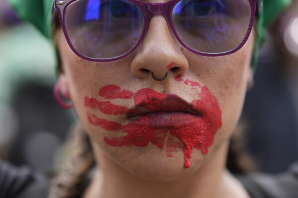 A woman attends an International Women's Day event with a red handprint across her mouth, a symbolic representation of murdered and missing Indigenous women, in Bogota, Colombia, Friday, March 8, 2024. (AP Photo/Fernando Vergara)