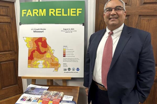 Missouri Treasurer Vivek Malek stands near a poster promoting drought conditions and state aid programs on Jan. 4, 2024, at his Capitol office in Jefferson City, Mo. Agricultural entities are among several categories of businesses that can receive low-interest loans backed by deposits of state funds made by the treasurer's office. Participation in such programs has grown in various states. (AP Photo/David A. Lieb)