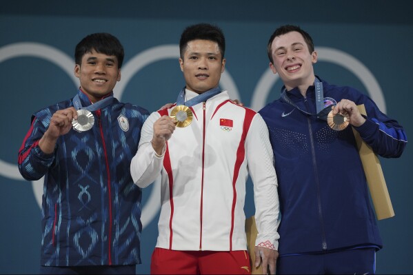 Medalist, from left to right, Theerapong Silachai of Thailand, silver, Li Fabin of China, gold, and Hampton Morris of the United States, bronze, celebrate on the podium during the medal ceremony for the men's 61kg weightlifting event at the 2024 Summer Olympics, Wednesday, Aug. 7, 2024, in Paris, France. (AP Photo/Kin Cheung)