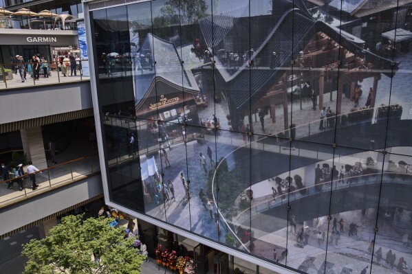 People tour by a projector screen promoting a newly opened outdoor Hutong style shopping mall, in Beijing, Monday, May 26, 2025. (AP Photo/Andy Wong)