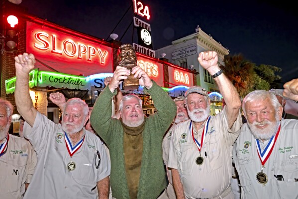 In this Saturday, July 22, 2023, photo provided by the Florida Keys News Bureau, Gerrit Marshall, center, hoists his trophy after winning the Hemingway Look-Alike Contest at Sloppy Joe's Bar in Key West, Fla. After 11 years of competing Marshall, a Madison, Wisc., resident, finally achieved success on his 68th birthday. Flanking Marshall, from left, are previous winners including Tom Grizzard, Wally Collins and John Stubbings. The competition was a highlight of the annual Hemingway Days festival that ends Sunday, July 23. Ernest Hemingway lived in Key West throughout most of the 1930s. (Andy Newman/Florida Keys News Bureau via AP)