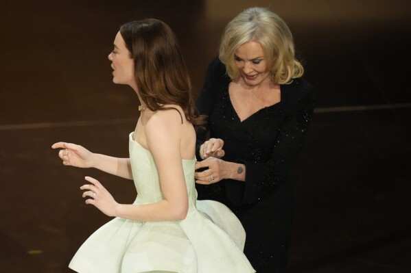 Jessica Lange, right, adjusts Emma Stone's dress during the Oscars on Sunday, March 10, 2024, at the Dolby Theatre in Los Angeles. (AP Photo/Chris Pizzello)