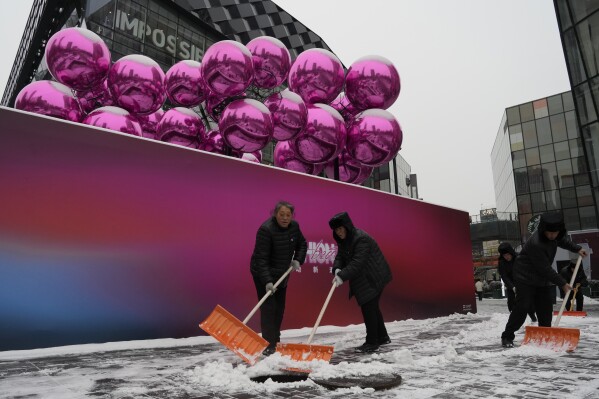 Workers sweep snow into a manhole near a decoration setup ahead of the Christmas festival at a mall in Beijing, Thursday, Dec. 14, 2023. China's economy will slow next year, with annual growth falling to 4.5% from 5.2% this year despite a recent recovery spurred by investments in factories and construction and in demand for services, The World Bank said in a report issued Thursday. (AP Photo/Ng Han Guan)
