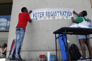 FILE - Aetry Jones, left, and Caerry Rigbon tape up a voter registration sign on Dallas City Hall before a Juneteenth 2020 celebration in Dallas on June 19, 2020. Social media users are falsely claiming that a "skyrocketing" number of unauthorized migrants are registering to vote in Arizona, Texas and Pennsylvania. (AP Photo/LM Otero, File)