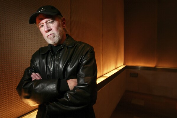 FILE - Actor and comedian George Carlin poses in a New York hotel March 19, 2004. Carlin's estate has filed a lawsuit against the media company behind a fake hourlong comedy special that purportedly uses artificial intelligence to recreate the late standup comic’s style and material. The lawsuit filed in federal court in Los Angeles on Thursday, Jan. 25, 2024, asks that a judge order the podcast outlet, Dudesy, to immediately take down the audio special, “George Carlin: I'm Glad I'm Dead,