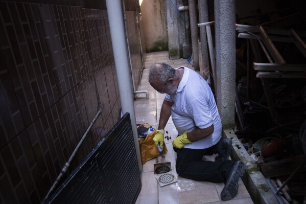 Augusto Cesar, a city worker who combats endemic diseases, pours larvicide down a home's drain where mosquitoes can breed, to help eradicate the Aedes aegypti mosquito which can spread dengue, in the Morro da Penha favela of Niteroi, Brazil, Friday, March 1, 2024. (APPhoto/Bruna Prado)