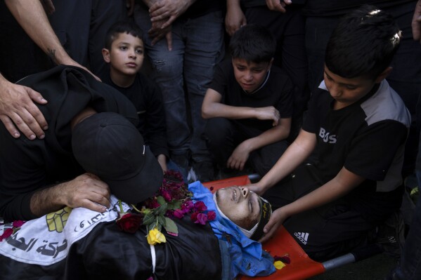 Relatives mourn over the body of a Palestinian man, draped in the Islamic Jihad militant group flags, during his funeral in the Nur Shams refugee camp, near the West Bank town of Tulkarem, Sunday, April 21, 2024. The Palestinian Red Crescent rescue service said 14 bodies have been recovered from the Nur Shams urban refugee camp since an Israeli military operation began in the area Thursday night. The Islamic Jihad militant group confirmed the deaths of three members. Another killed was a 15-year-old boy. The Israeli army said its forces killed 10 militants in the camp and surrounding areas while eight suspects were arrested. (AP Photo/Nasser Nasser)