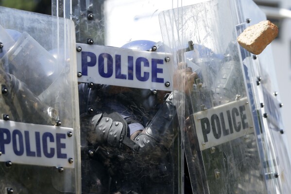 FILE - Riot police officers shield off stones thrown by students during their protest against university tuition hikes outside the union building in Pretoria, South Africa, Friday, Oct. 23, 2015. Eight police officers assigned to a security team protecting South Africa’s deputy president have been arrested and are expected to appear in court on Monday, July 24, 2023 after they were caught on video kicking and stomping on two men on a Johannesburg highway this month. One of the men was kicked unconscious in the attack. (AP Photo/Themba Hadebe, File)
