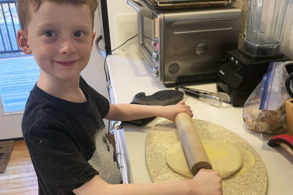 This March 22, 2020, photo released by Alexandra Nicholson shows her son, Henry Martinsen, making food in Quincy, Mass. The frustration of parents is mounting as more families across the U.S. enter their second or even third week of total distance learning, and some say it will be their last. (Alexandra Nicholson via AP)